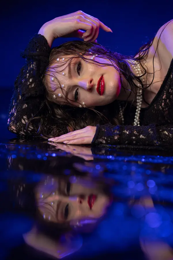 Woman reclining on a reflective surface under blue light