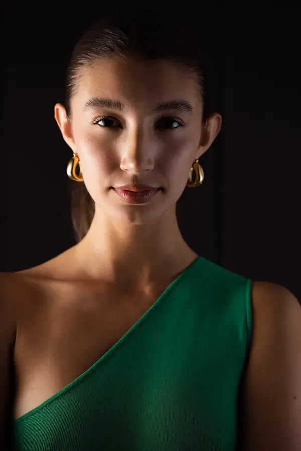 Low-key studio headshot of a woman in a green one-shoulder dress