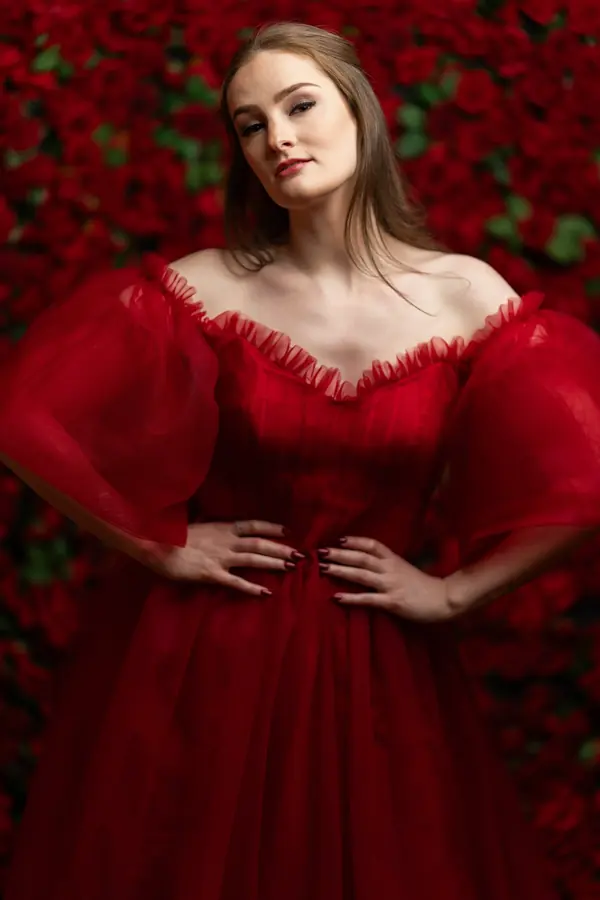 Woman in a red tulle gown in front of a wall of red roses